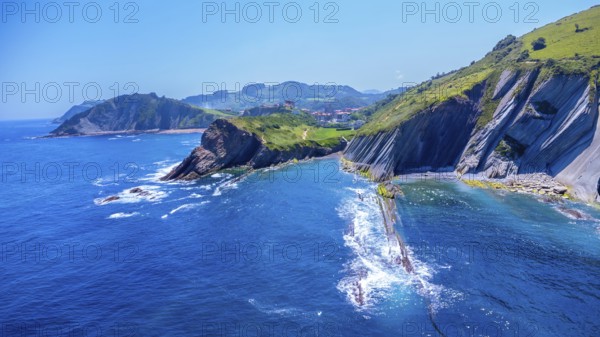 Breathtaking aerial view of the unique flysch cliffs meeting the deep blue water of the cantabrian sea on a sunny summer day in zumaia, gipuzkoa, spain.