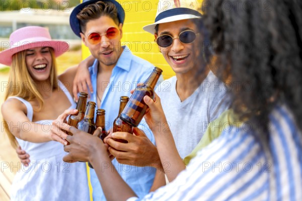 Cheerful multi ethnic friends enjoying a summer party, toasting with beer bottles against a vibrant yellow wall