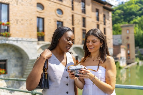 Two happy female tourists reviewing photos on a vintage camera while visiting the historic city of albi, france