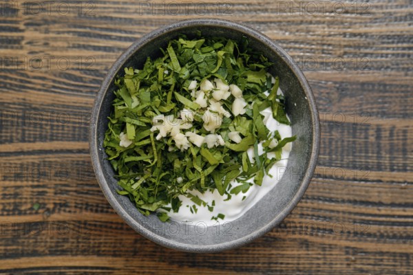 Freshly chopped herbs, including parsley and garlic, are mixed with creamy yogurt in a rustic kitchen. This traditional dish preparation captures the essence of making dolma at home