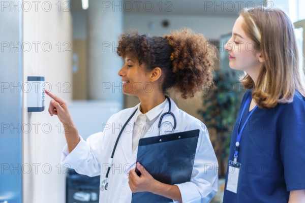 Female doctor entering security pin code on keypad access control, next to a nurse, in a hospital corridor