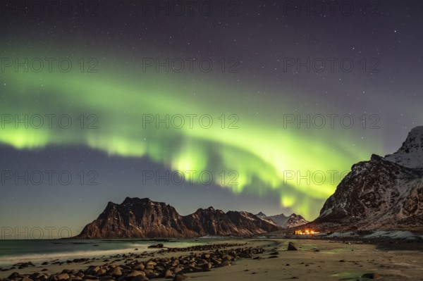 Aurora borealis in green colors over mountain range and coastline at night, Lofoten, Norway