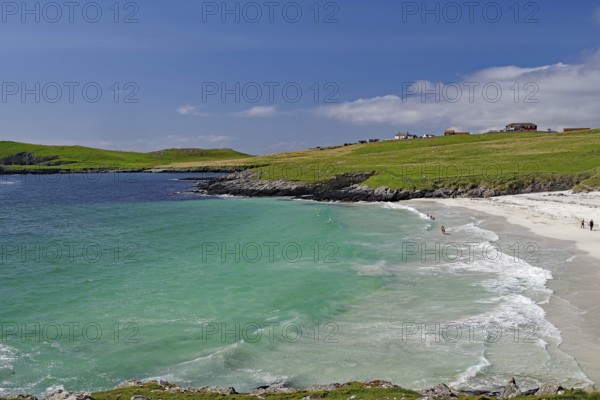 A picturesque beach with turquoise waters and gentle waves under a blue sky, surrounded by green hills and scattered houses, Meal Beach, Scalloway, Shetland Islands, Scotland, United Kingdom