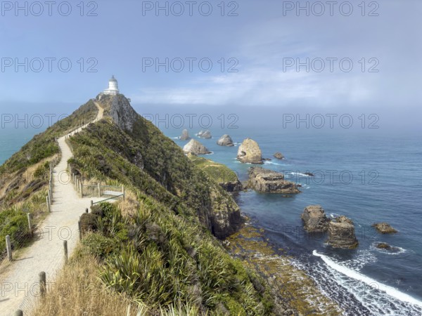 Nugget Point Lighthouse with Nugget Rocks in front of a blue sky, South Island, New Zealand, Oceania