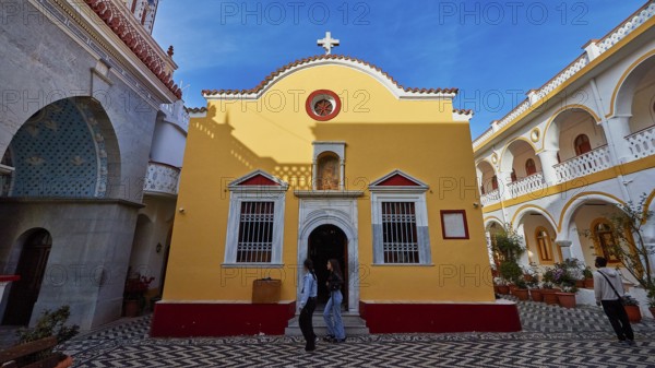 Yellow baroque-style church with cross and floor pattern in the courtyard, Holy Week, Panormitis Bay, Panormitis Monastery, Symi, Dodecanese, Greek Islands, Greece
