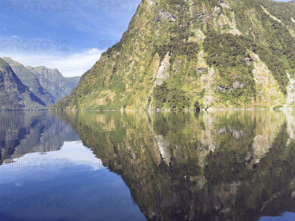 Mountains with reflections in the water against a blue sky in Doubtful Sound, South Island, New Zealand, Oceania