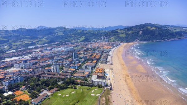 Aerial perspective of zarautz, gipuzkoa, showcasing the urban landscape meeting the sandy beach and blue ocean waves under a clear summer sky, Spain.