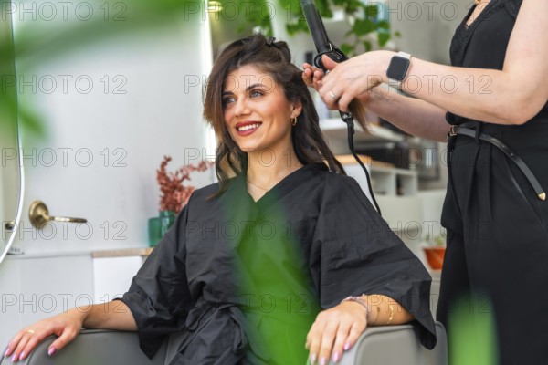 Hairdresser styling hair of a smiling client with a curling iron in a chic, modern beauty salon, creating a stunning hairstyle