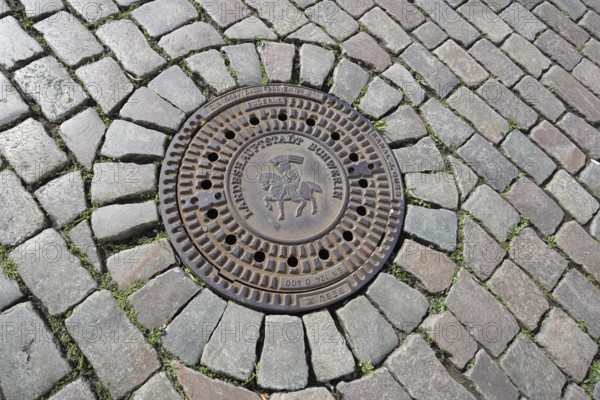 Round manhole cover with city coat of arms and inscription, state capital, paving stones, floor, Schwerin, Mecklenburg-Vorpommern, Germany