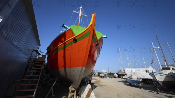 Frontal view of a ship's bow in orange and green on a shipyard site, Diakofti boatyard, new construction of a coloured wooden boat, Diakofti, Patmos, Dodecanese, Greek Islands, Greece