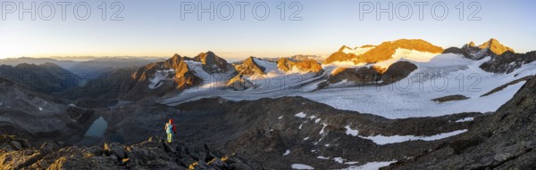 Mountaineer in front of picturesque high mountain landscape at sunrise with alpenglow, blue glacial lakes, glaciers and rocky mountain peaks in the morning light, view at the Becher on mountain peaks Königshofspitz and Sonklarspitze and Schwarzwandspitz with glacier Übeltalferner, Stubai Alps, South Tyrol, Italy