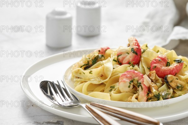 A plate of fettuccine allo Scoglio features fresh pasta topped with shrimp, mussels, and herbs, showcased in an inviting dining environment with minimalistic decor focused on the dish