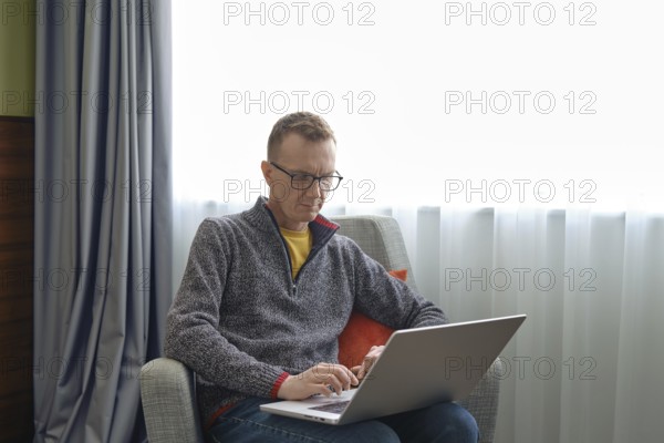 A middle-aged man sits comfortably in an armchair and watching as real estate agent showing a property through an online video call