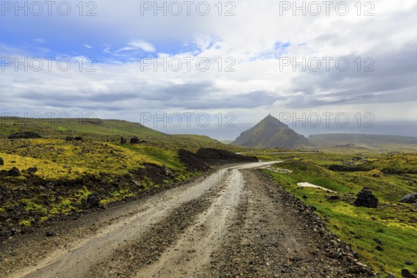Gravel track through barren moss-covered volcanic landscape, cone-shaped mountain Stapafell, rain clouds, changeable weather, Arnarstapi, Snaefellsjökull volcanic system, Snaefellsnes peninsula, West Iceland, Iceland