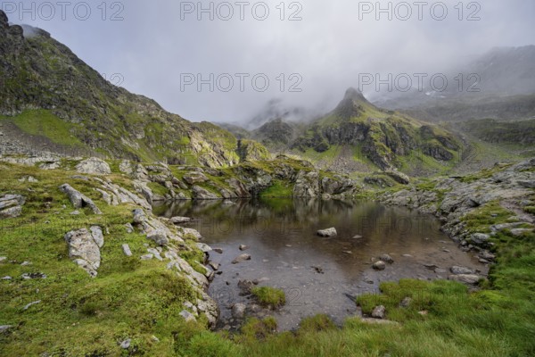 Small mountain lake, cloudy mountain peaks reflected in the lake, Schober group, Hohe Tauern National Park, Carinthia, Austria