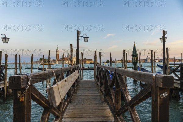 Wooden pier with gondolas and lamps leading to san giorgio maggiore in venice at sunset, creating a romantic and picturesque view