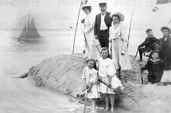 Family on the beach, 1910s, Victorian beach shot of a family with children next to a sailing boat in the background, historical photo