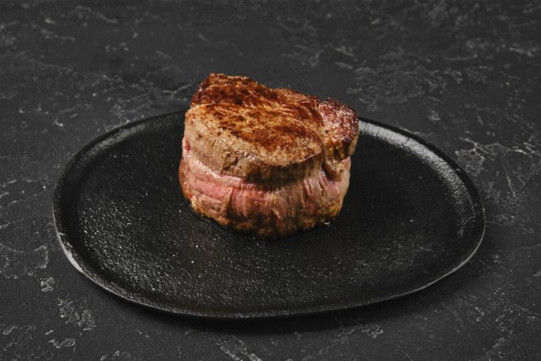 Perfectly seared filet mignon sits on a dark plate, highlighting its rich color and inviting look. The meat exhibits a mouthwatering crust, promising a tender and flavorful experience for diners