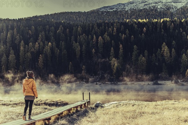 Young woman at Lake Staz near Sankt Moritz in the Engadine in Switzerland. Morning atmosphere with fog in autumn. Reflection of water