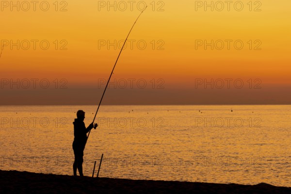 A man fishing just in front of sunrise on the Costa Rei, a coastline of the Italian island of Sardinia, in the Mediterranean Sea, Monte Nai, Costa Rei, Sardinia, Italy