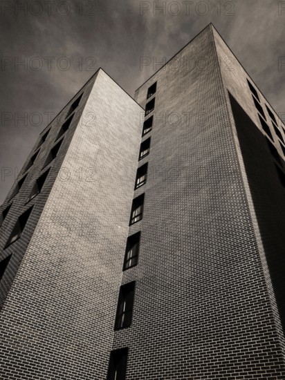 A striking building features unique geometric shapes and intricate brickwork, towering high against a moody sky in a contemporary urban setting. Large windows add to its modern appeal. France