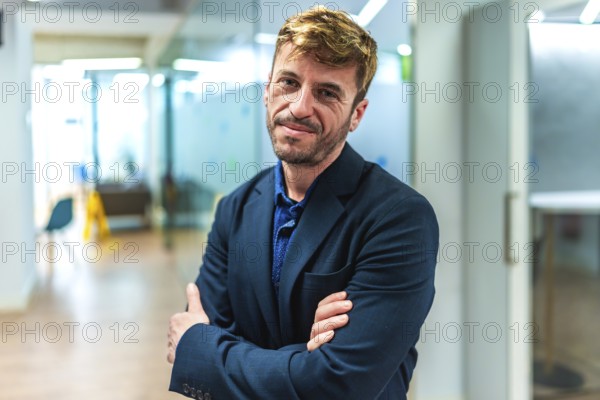 Portrait of a smiling businessman standing with crossed arms in a modern office, exuding confidence and professionalism