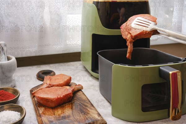 Thick pork rib chops are being cooked in an air fryer, showcasing the ease of preparing tender meat at home. Seasonings are prepared on the side for added flavor in this culinary activity