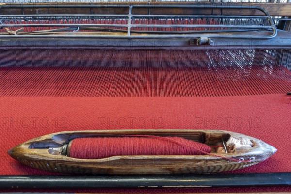 Old loom in the clothmaking museum in Bramsche, Lower Saxony, Germany, wooden shuttle on red fabric on a loom