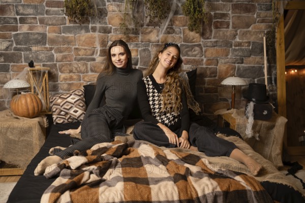 Two women enjoy a relaxed moment together on a warm blanket in a rustic bedroom filled with autumn decor