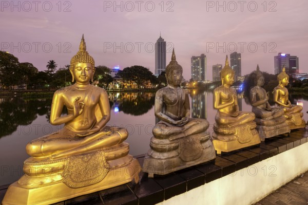 Buddha statues of Seema Malaka Temple at Beira Lake at sunset, Colombo skyline behind, Sri Lanka