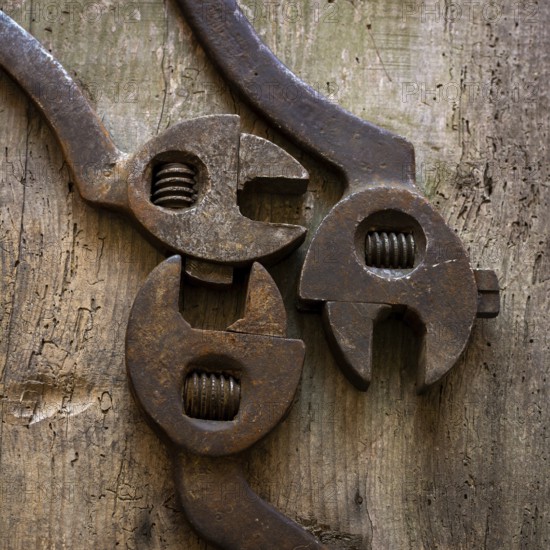 Three vintage hand tools, including adjustable wrenches, rest on a rustic wooden workbench. The tools show signs of wear, reflecting their long history and practical use in craftsmanship