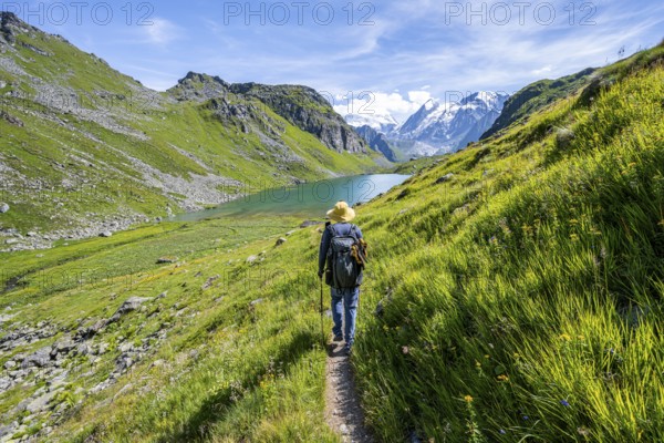 Mountaineer on hiking trail in picturesque mountain landscape, view of mountain lake Lac du Louvie and glaciated mountain peaks of the Grand Combine, Valais Alps, Val de Bagnes, Valais, Switzerland