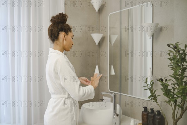 A young woman wearing a white bathrobe stands at a sleek sink in a stylish bathroom