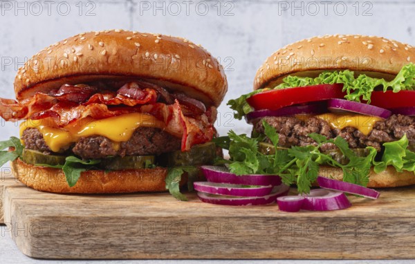 Two burgers with beef patty, fried bacon, cheddar cheese, tomatoes, on a light table