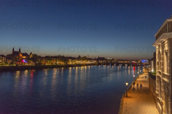 Maastricht, Netherlands, night view of the river Maas with illuminated bridge and promenade, under a clear sky