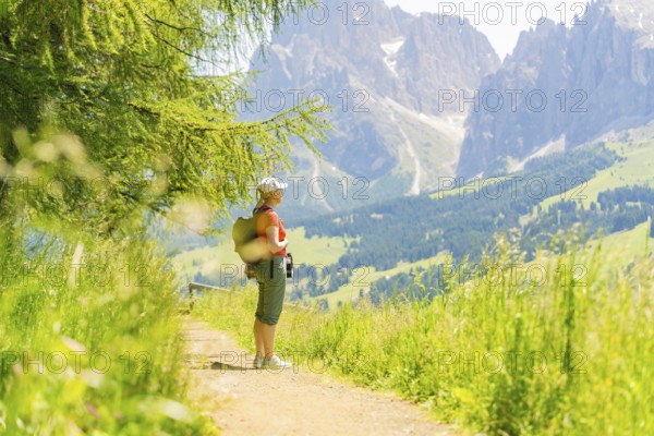 Person walking on a path with a view of mountains on a sunny day, Alpe di Siusi, Dolomites, South Tyrol, Italy