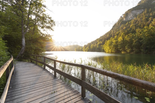 Sunrise in summer at Lake Thumsee near Bad Reichenhall with a wooden footbridge and a sun star over the lake