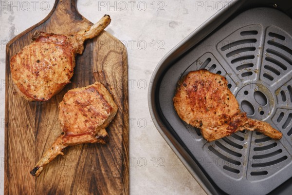 Juicy pork rib roasts are beautifully cooked to perfection, resting on a wooden cutting board. An air fryer sits nearby, ready for additional cooking or meal prep