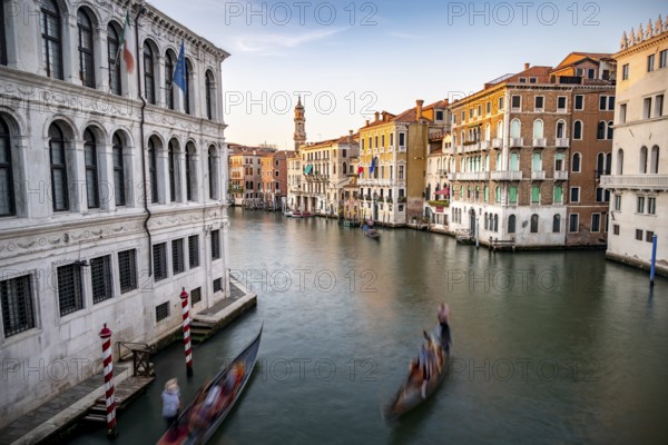 View of the Grand Canal with gondoliers at sunset, picturesque evening mood with palazzos on the canal and church tower of the Chiesa Parrocchiale dei Santi Apostoli, long exposure, view from the Rialto Bridge, Venice, Veneto, Italy