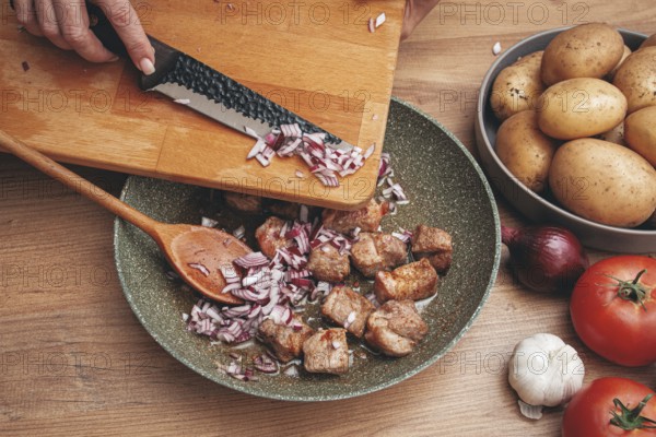 Adding chopped onion to the pan with meat, close-up