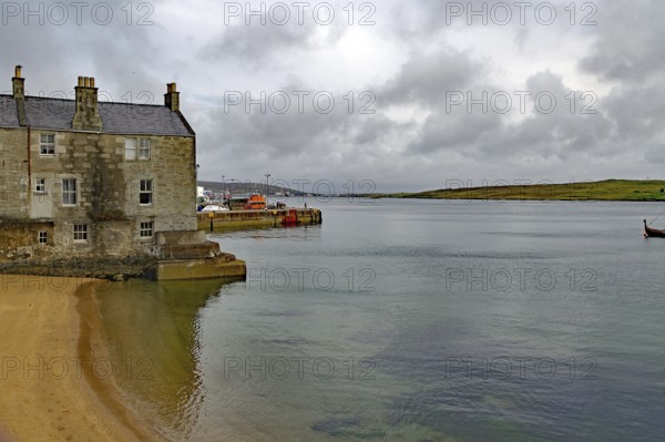 A stone cottage stands on the sandy shore of a calm loch under a cloudy sky, Lerwick, crime series, Shetland Islands, Scotland, United Kingdom