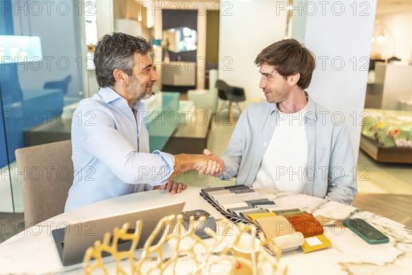 Interior designer shaking hands with a client in a furniture store showroom after choosing upholstery and fabric swatches