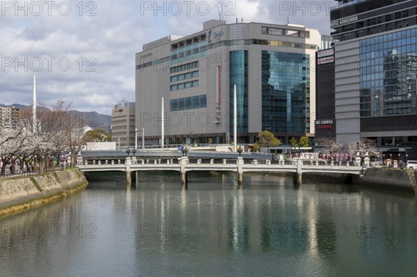 Tourist attraction, place of interest, riverside promenade with blossoming cherry trees, Sakura, modern architecture and historic Enkobashi stone bridge over the Enko River, Enko-bashi Bridge, built in 1926, restored in 2016 for the 70th anniversary of the atomic bombing, Enkobashicho, Minami Ward, Hiroshima, Japan