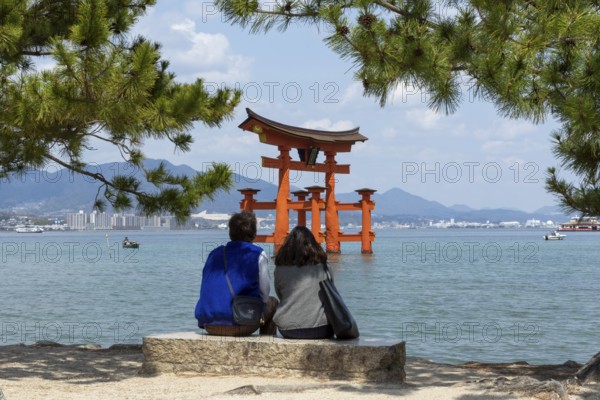 A couple on the beach looking at the torii in the water, landmark, tourist attraction, UNESCO World Heritage Site, Itsukushima Shrine, Miyajima Island, Hatsukaichi, Hiroshima Prefecture, Japan