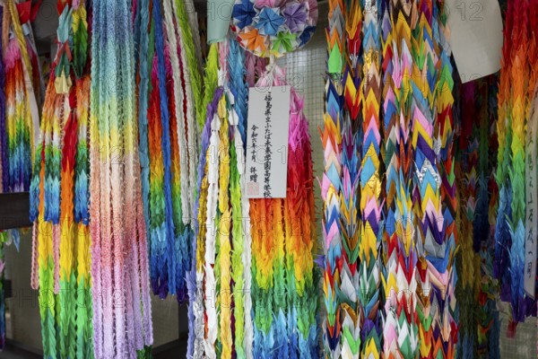 Chains of colourful origami cranes made of paper as a sign of peace in the Peace Park, landmark, UNESCO World Heritage Site, peace monument and memorial to the victims of the atomic bombing of Hiroshima, Naka Ward, Hiroshima, Japan