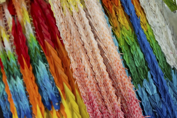 Chains of colourful origami cranes made of paper as a sign of peace in the Peace Park, close-up, background image, landmark, UNESCO World Heritage Site, peace memorial and memorial to the victims of the atomic bombing of Hiroshima, Naka Ward, Hiroshima, Japan
