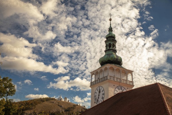A church tower with a clock sits enthroned against a cloudy sky and overlooks a hill, Mikulov Nikolsburg Czech Republic