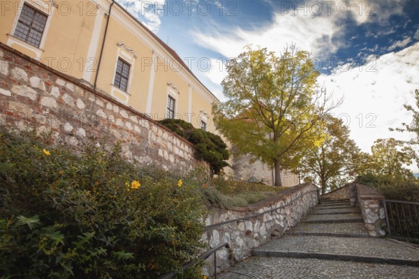 An idyllic path with stone steps and autumn trees leads to a yellow building, Mikulov Nikolsburg Czech Republic