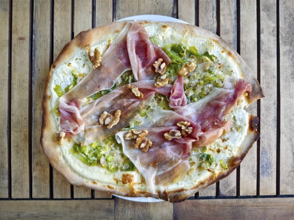 A gourmet pizza tarte flambée with raw ham and walnuts served on a wooden board, Lower Austria Austria