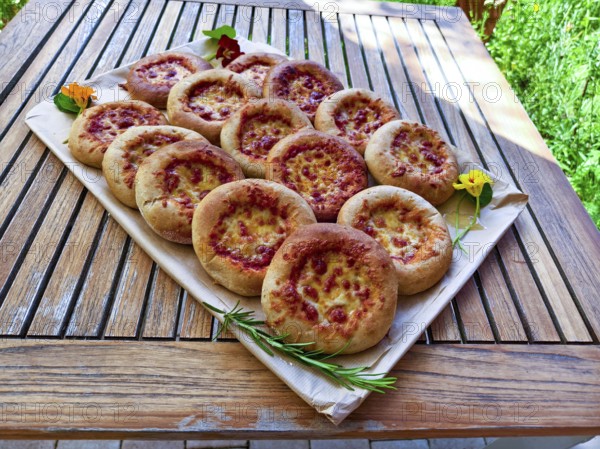 Several small pizzas on a wooden board decorated with flowers, presented on a garden table, Lower Austria Austria